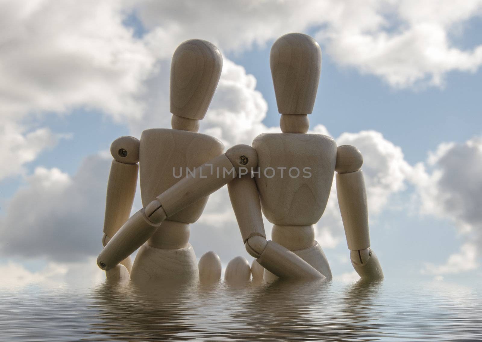 two wooden puppets as loving couple outside in the water with blue sky