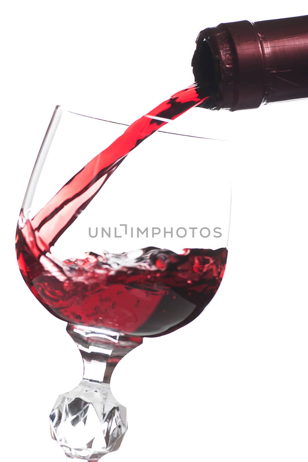 Red wine pouring down from a bottle into a glass over white background
