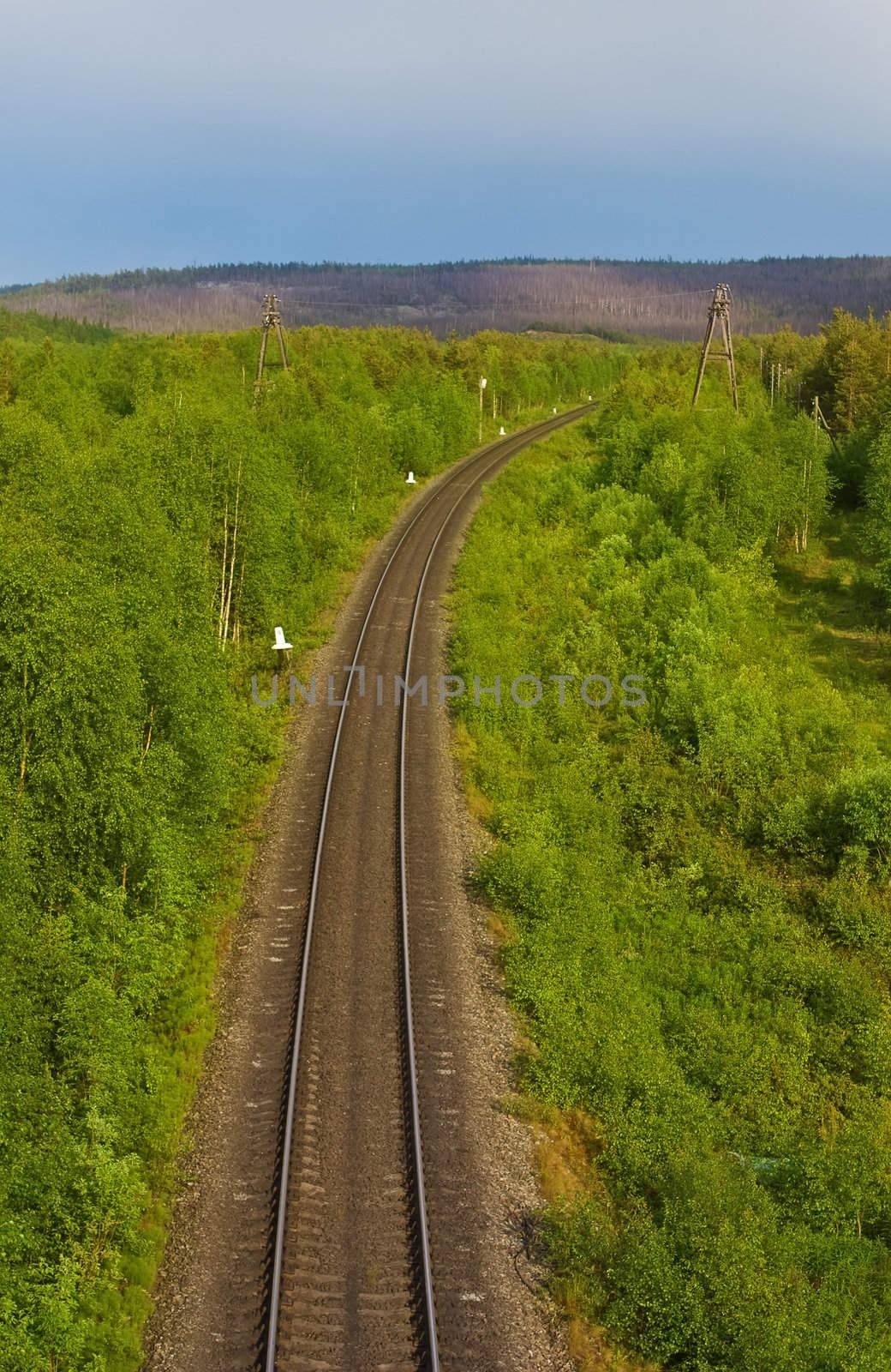 The railway turns to the right between green wood hills