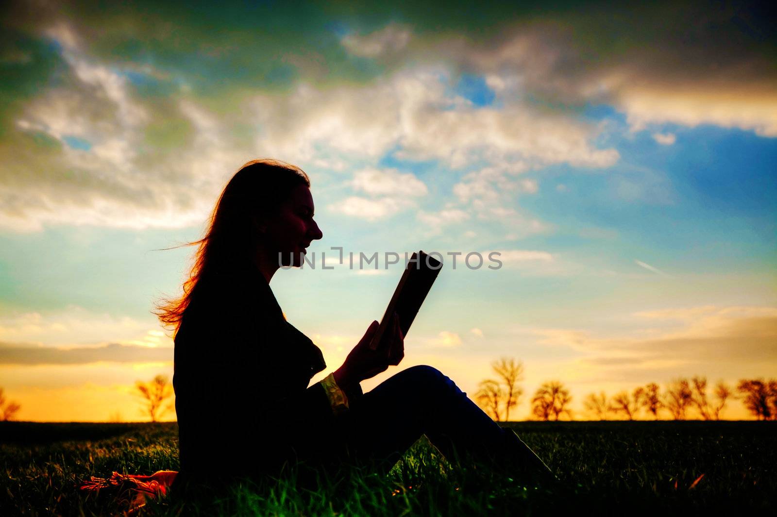 Teen girl reading book outdoors at sunset time