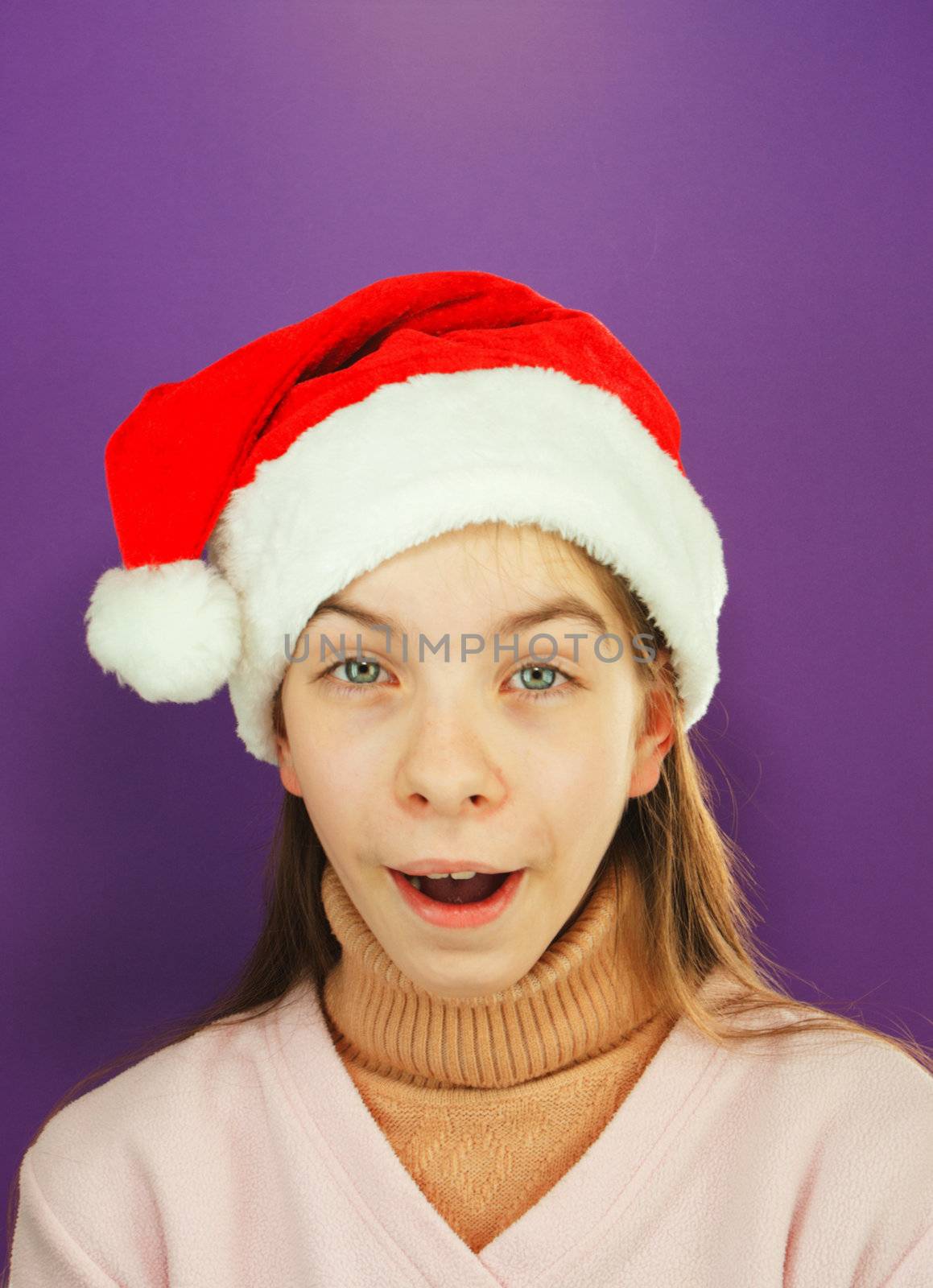 Pretty Santa girl, closeup portrait of a teen girl wearing Christmas hat against purple background
