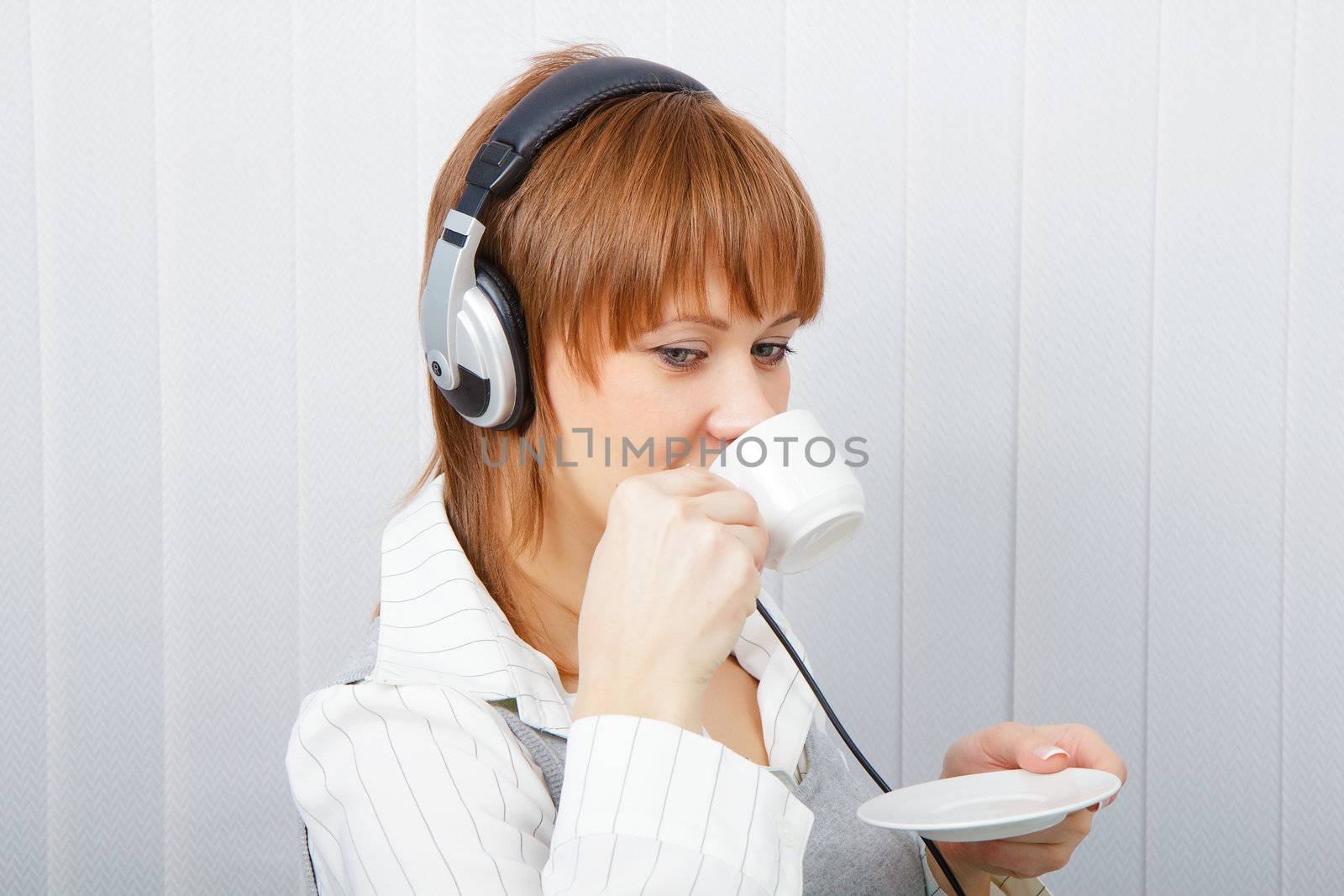The girl in headphones with a microphone drinks coffee