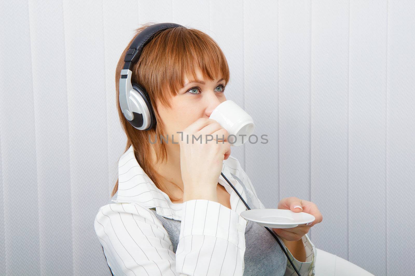 The girl in headphones with a microphone drinks coffee