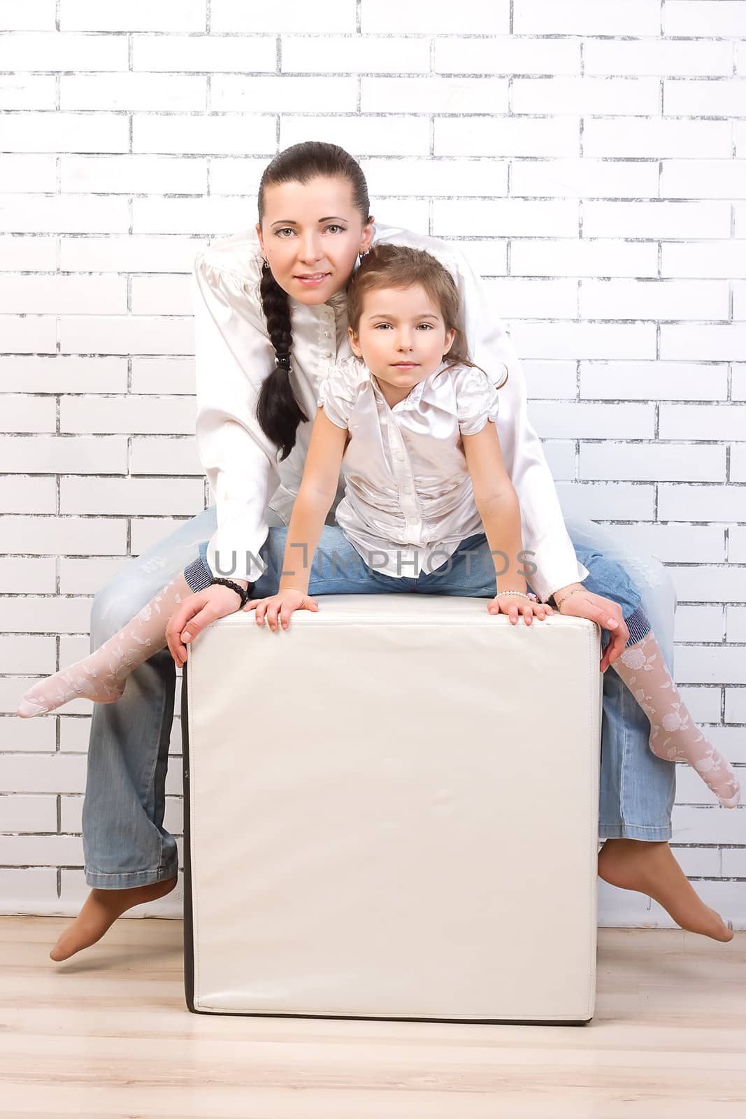 Mom and daughter in jeans and white shirt sitting in a chair in the shape of a cube