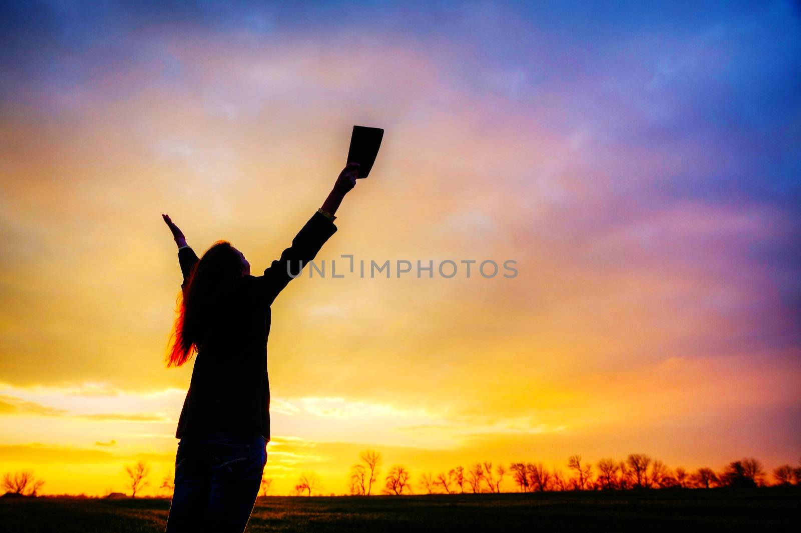 Woman staying with raised hands at the sunset time