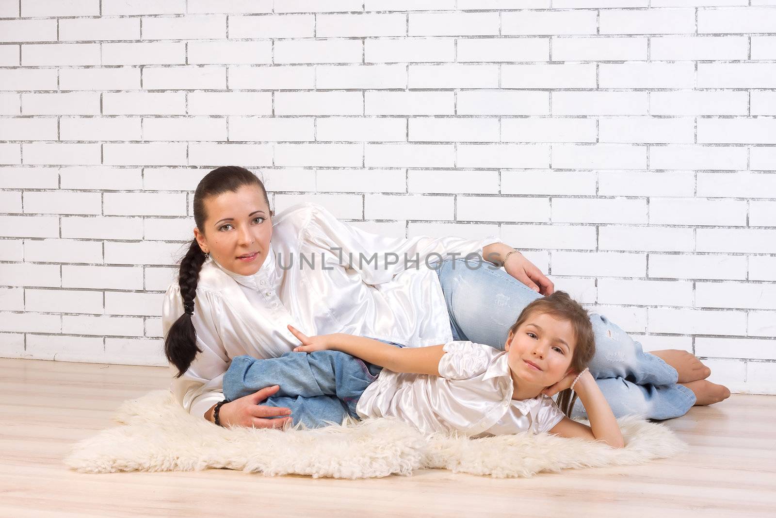 Mother and 5 year old daughter lie on white fur carpet