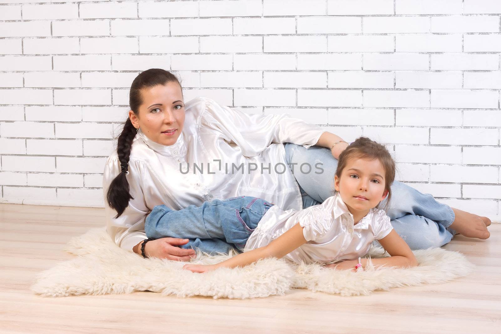 Mother and daughter lying on fur rug at home by victosha