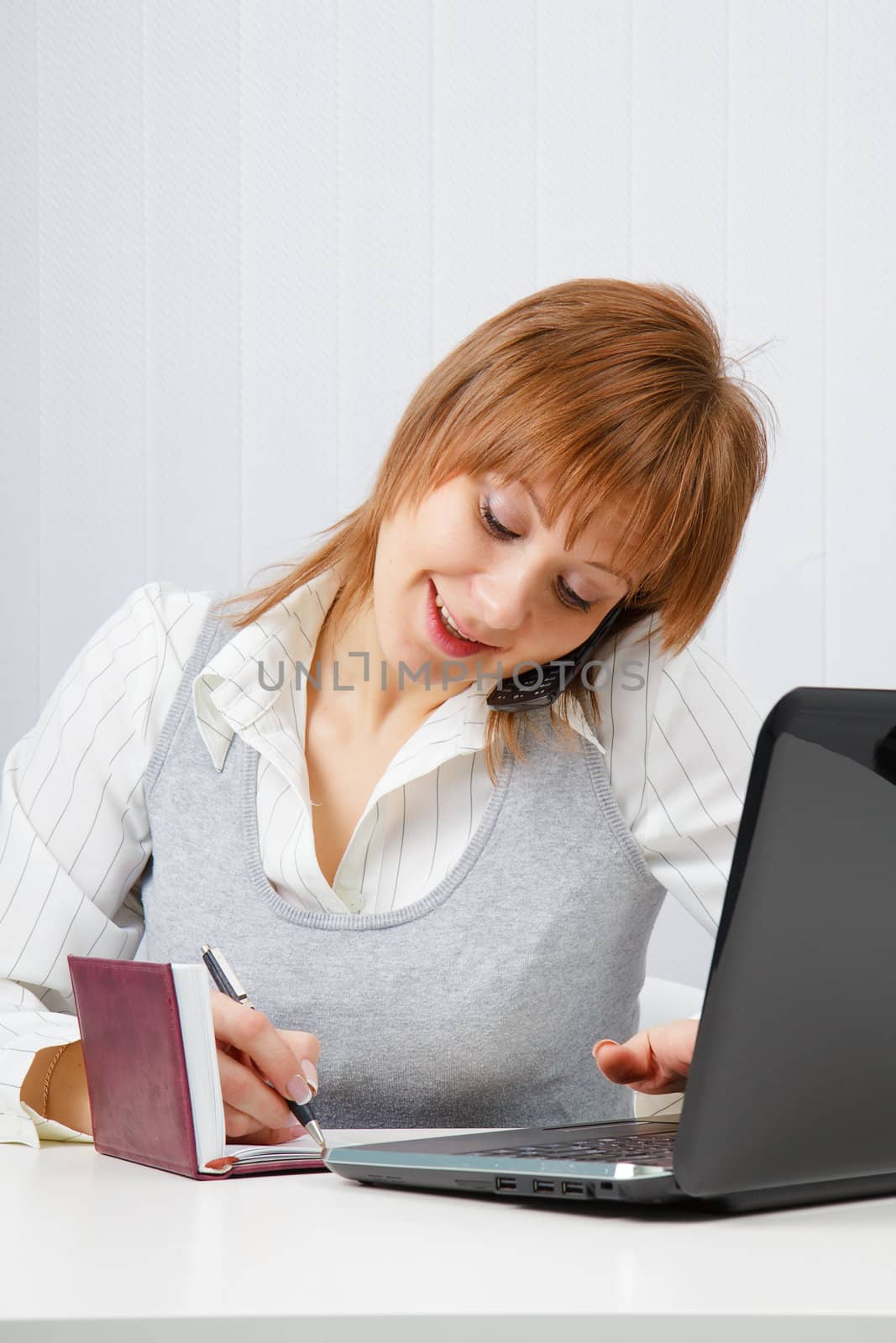 Attractive happy girl talking on the phone and writes simultaneously