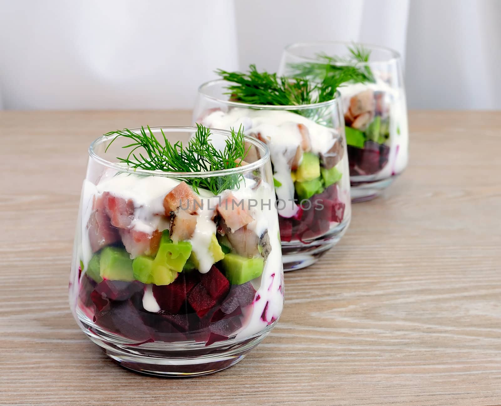 Beetroot salad with avocado and herring in cream sauce in a glass