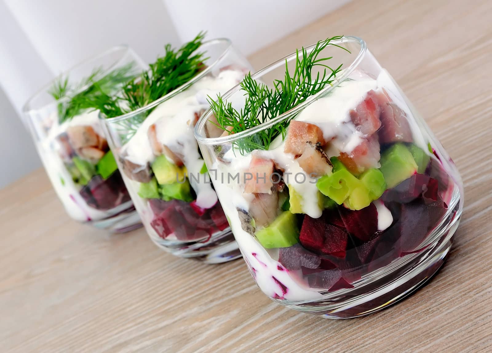 Beetroot salad with avocado and herring in cream sauce in a glass