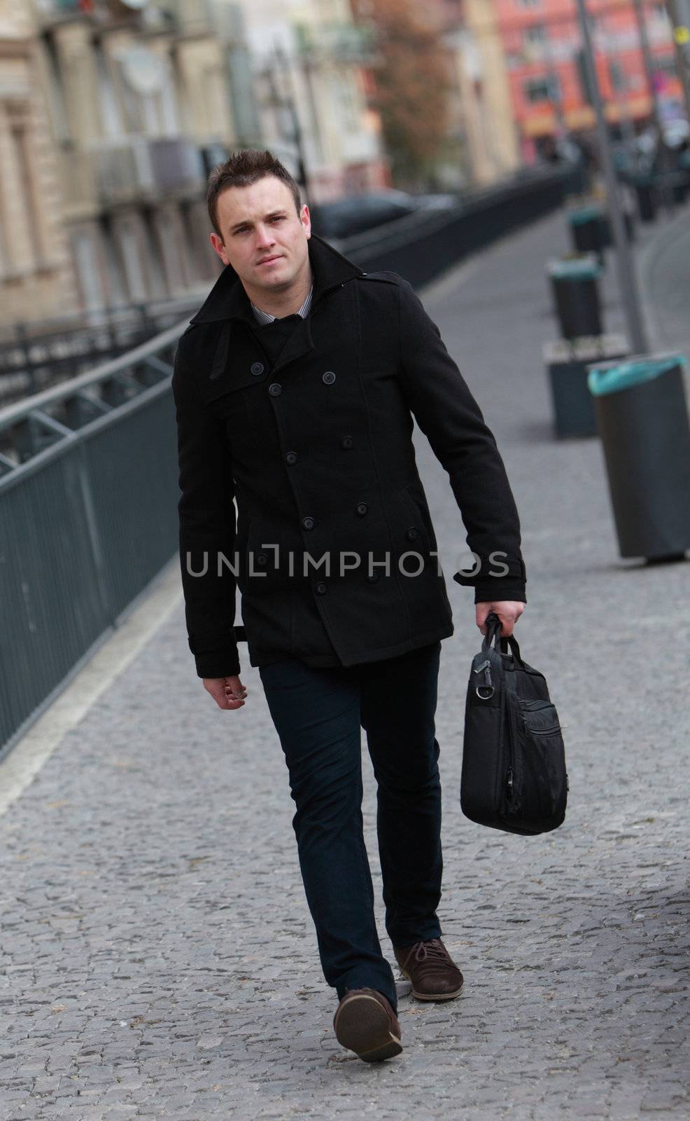 Image of a young businessman walking in cobbled street in a city.