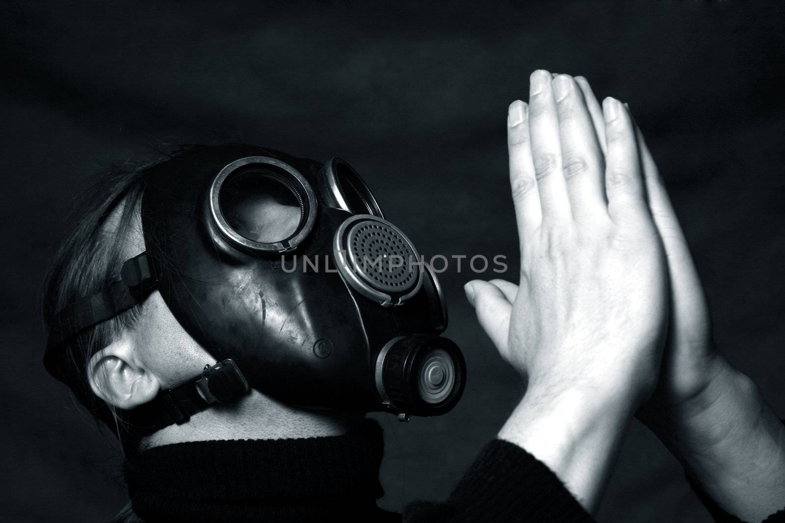 The man in a gas mask on a dark background. Hands are combined as at prayer