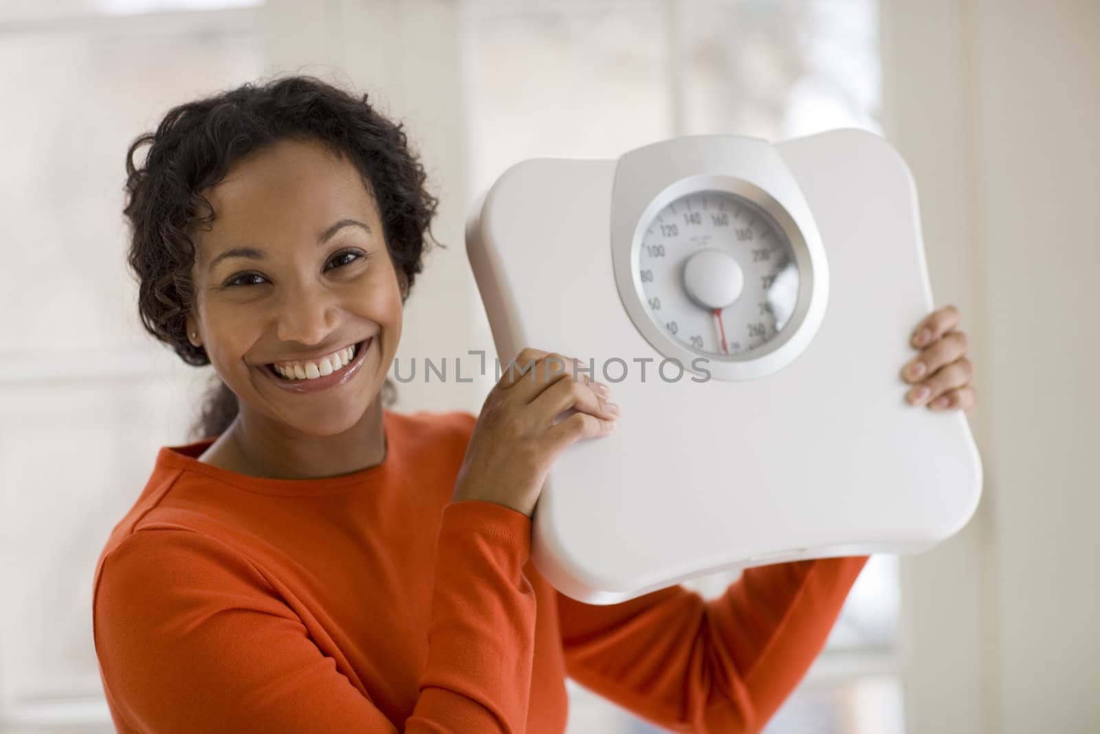 Happy Black woman holding scale by edbockstock