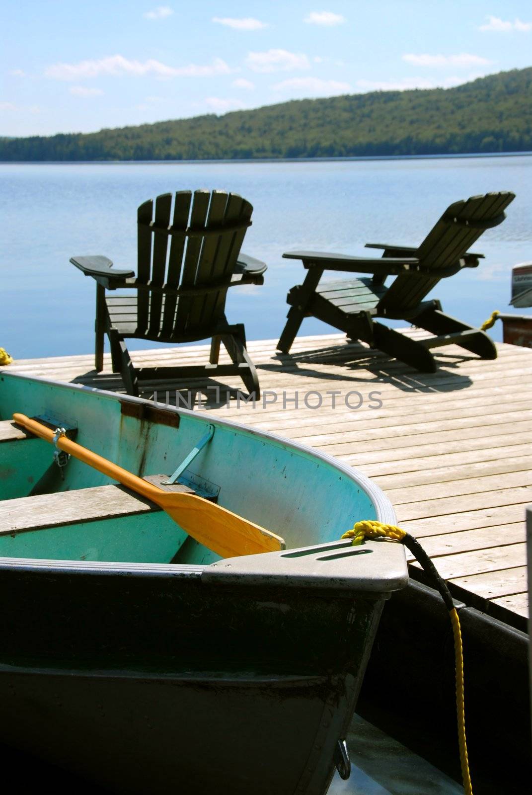 Paddle boat and two adirondack wooden chairs on dock facing a blue lake