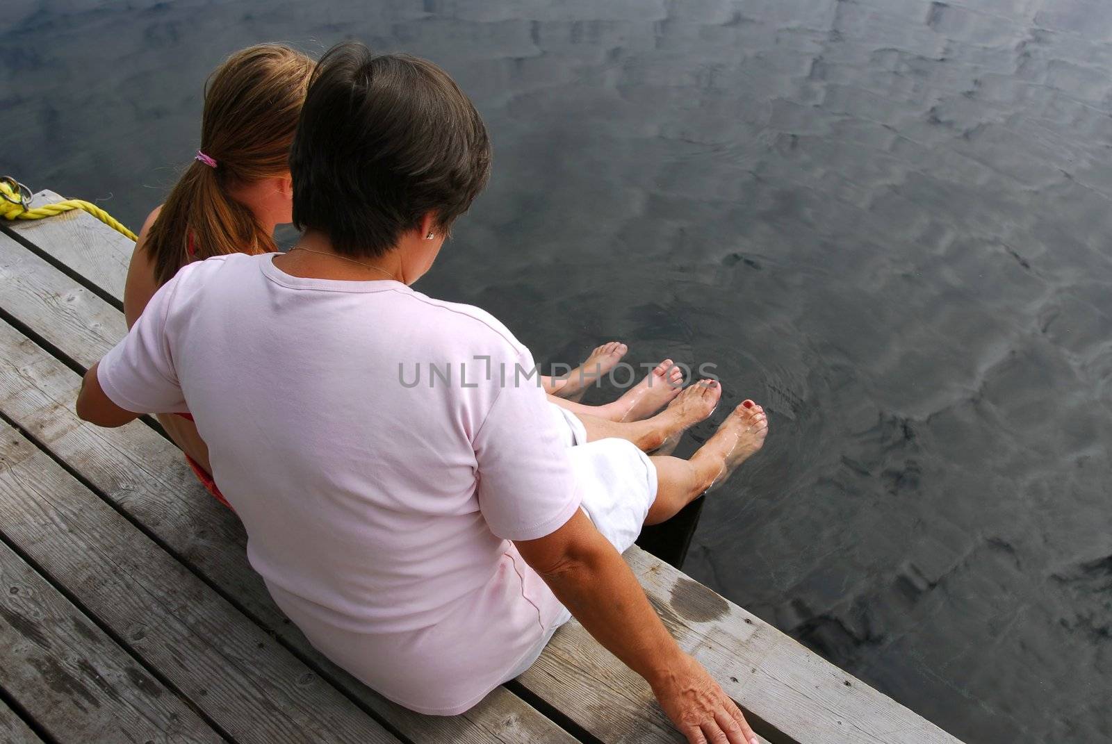Grandmother and granddaughter sitting on boat dock and dipping feet in water