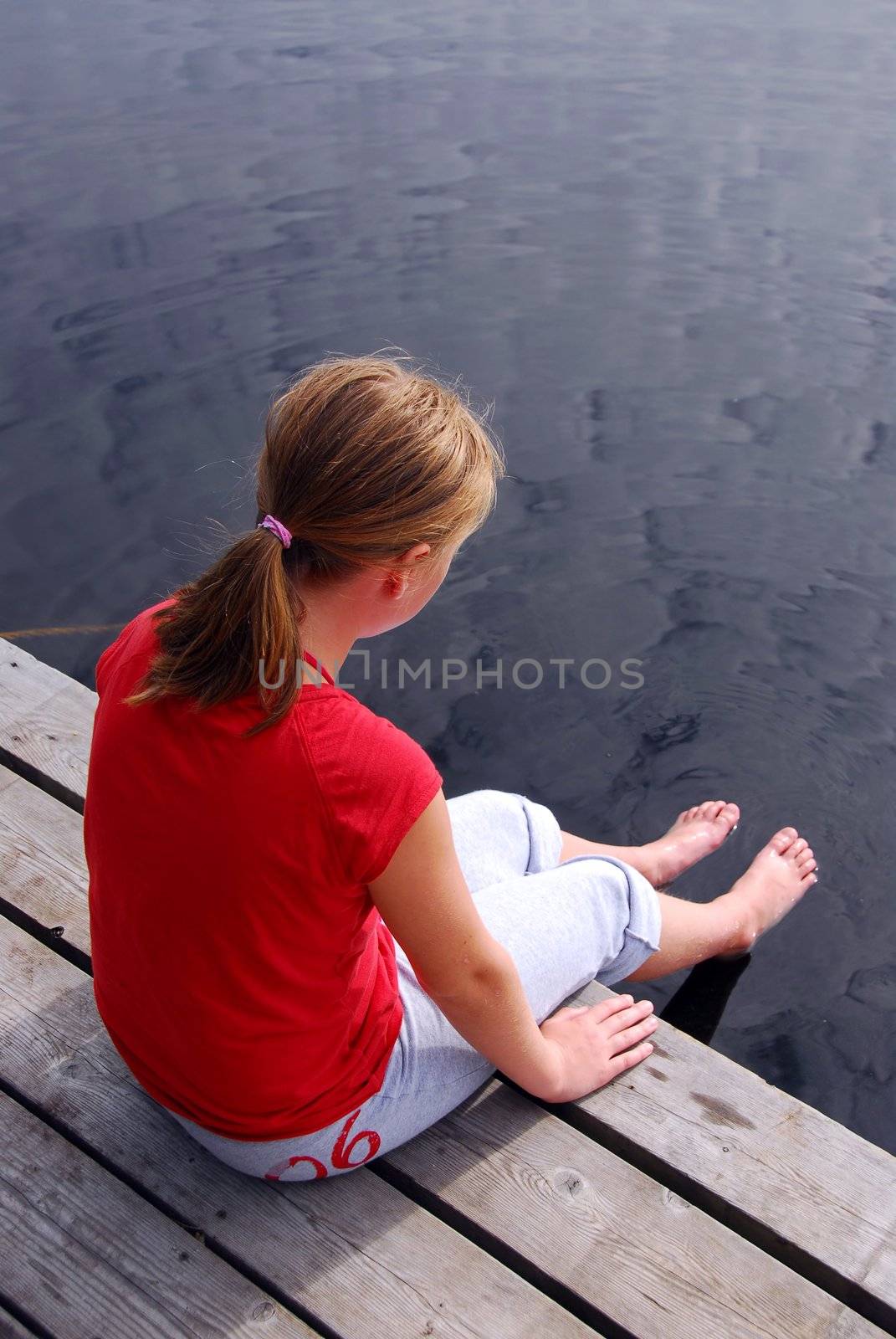 Young girl sitting on the edge of boat dock dipping her feet in water