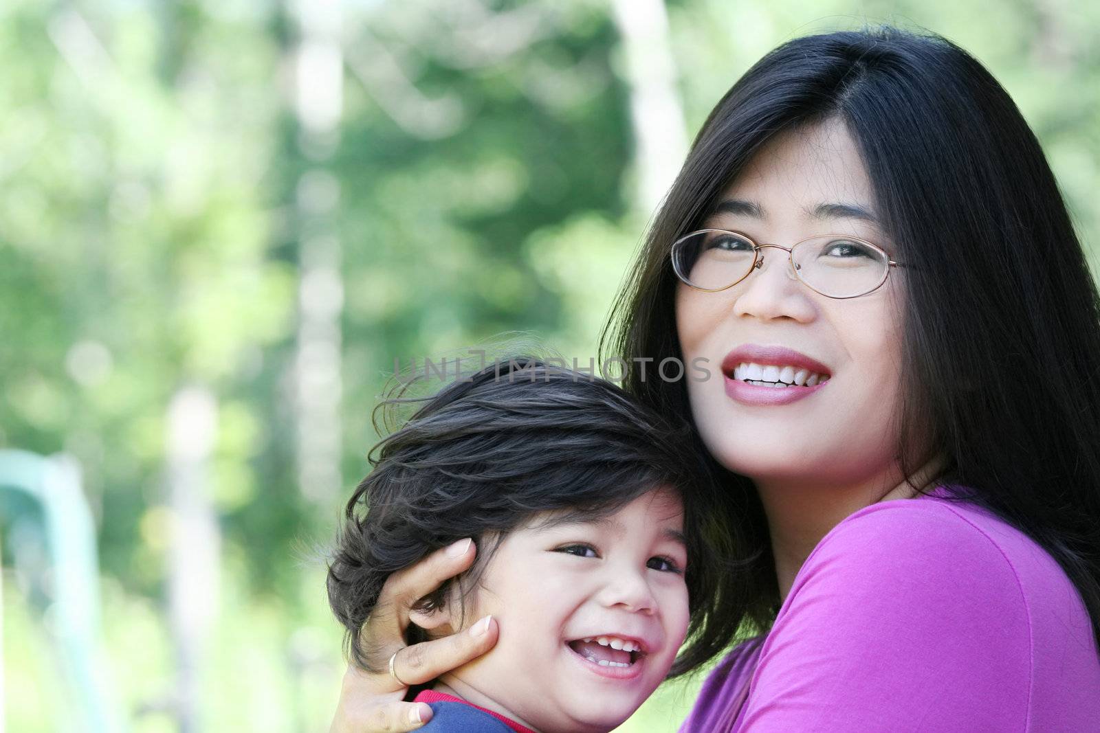 Asian mother lovingly holding her disabled son outdoors in summer. Child is biracial, asian caucasian background.