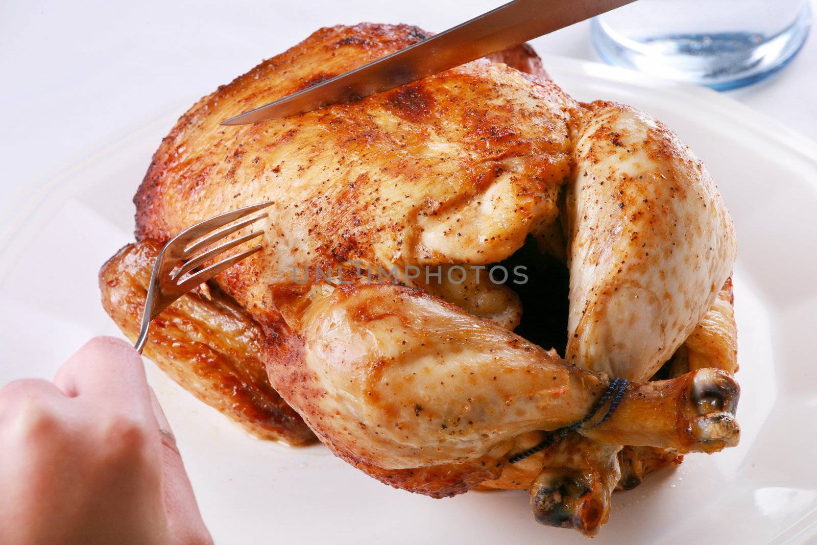 Hands carving rotisserie chicken with fork and knife