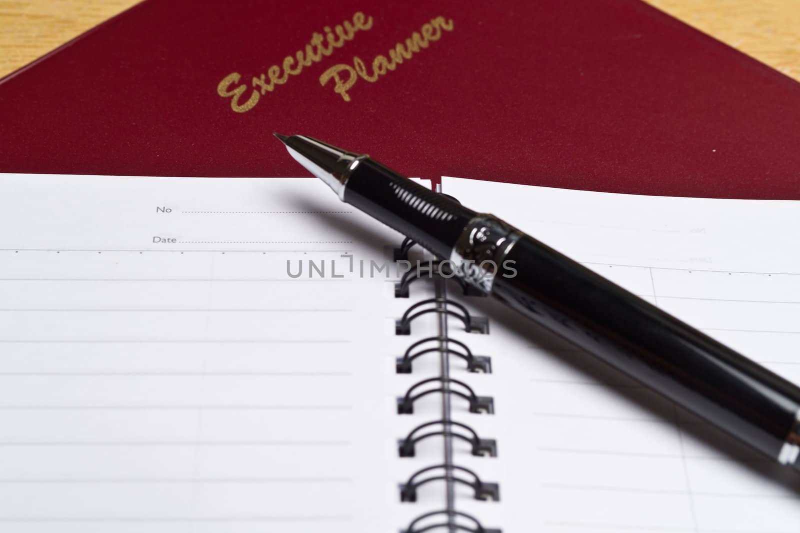 angled view of a  dark red executive planner with spiral note book and a pen in lanscape orientation