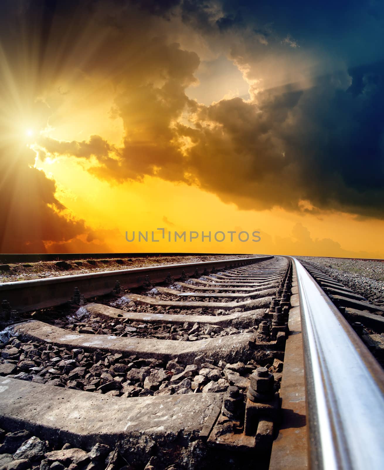 railway to horizon under dramatic sky with sun