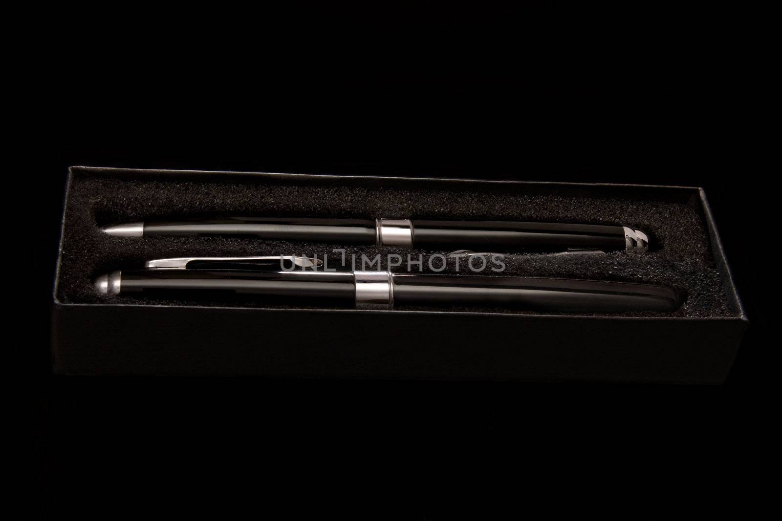 Two black pens in a black case on a black background