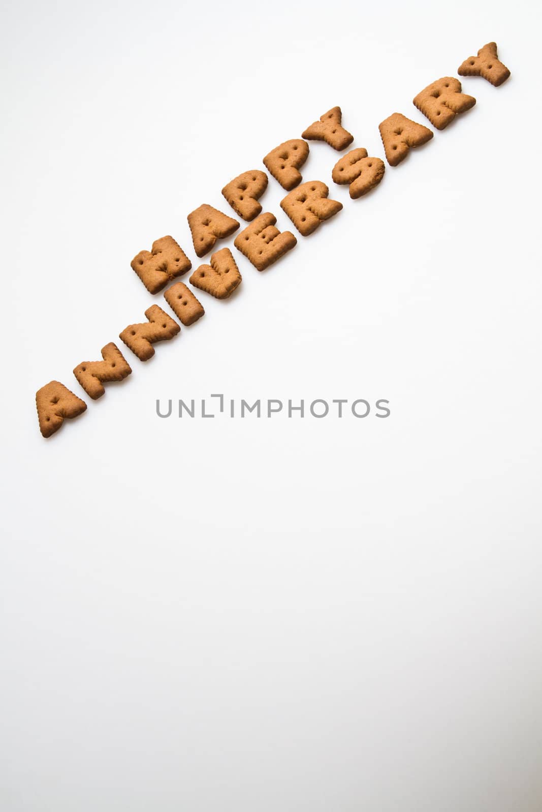 Happy anniversary wording made by brown biscuits slanting on white surface in portrait orientation