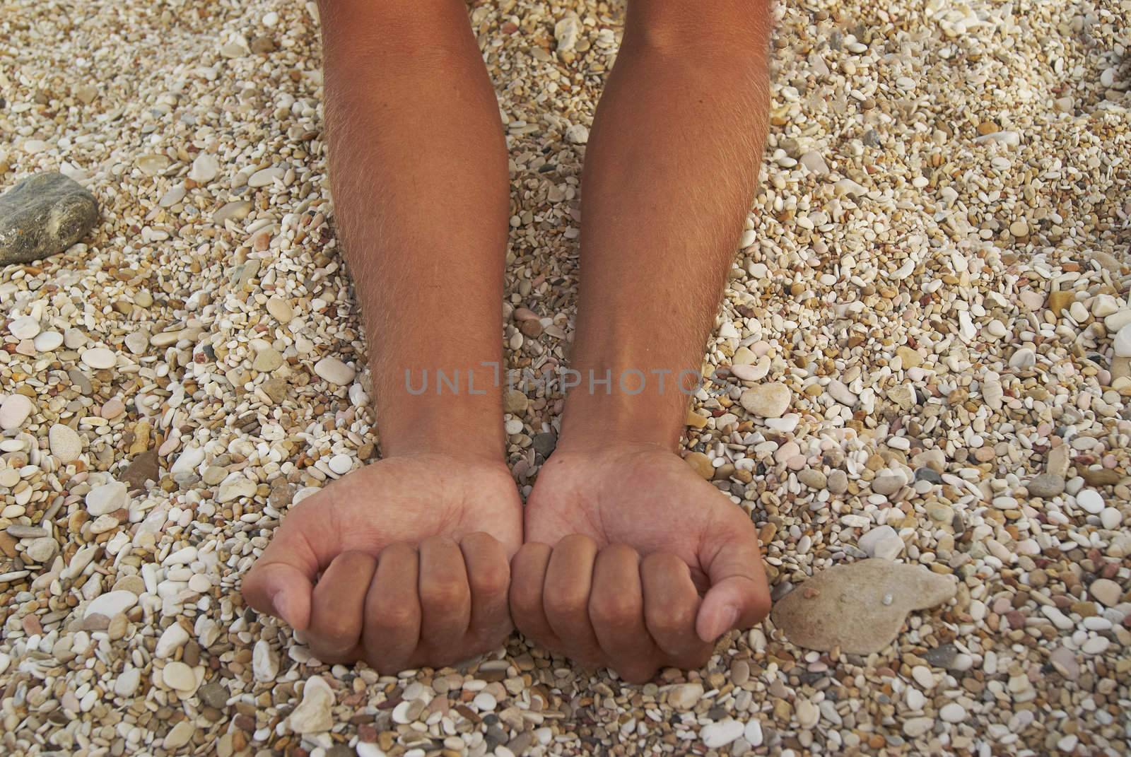 Man tanned hands compressed into cams against background of small stones on the beach