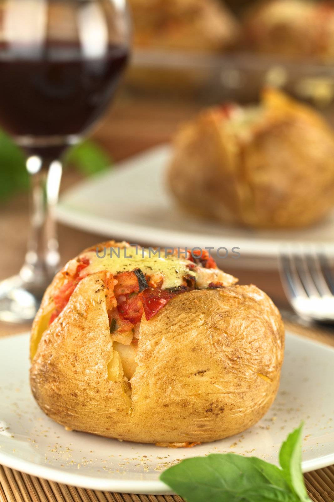 Baked potato with tomato filling and cheese on top with red wine in back (Selective Focus, Focus on the front of potato)