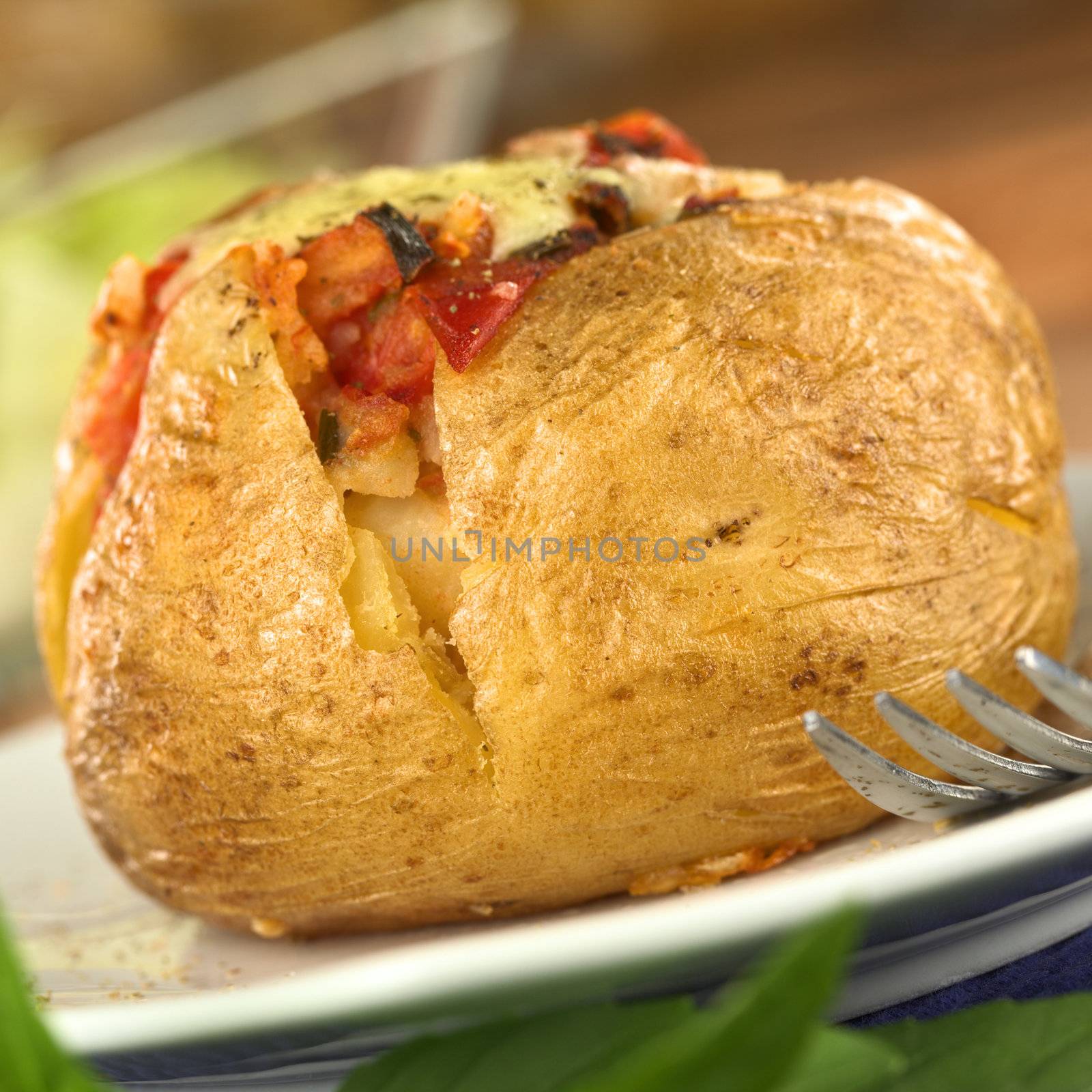 Baked potato with tomato filling and cheese on top (Selective Focus, Focus on the front of potato)