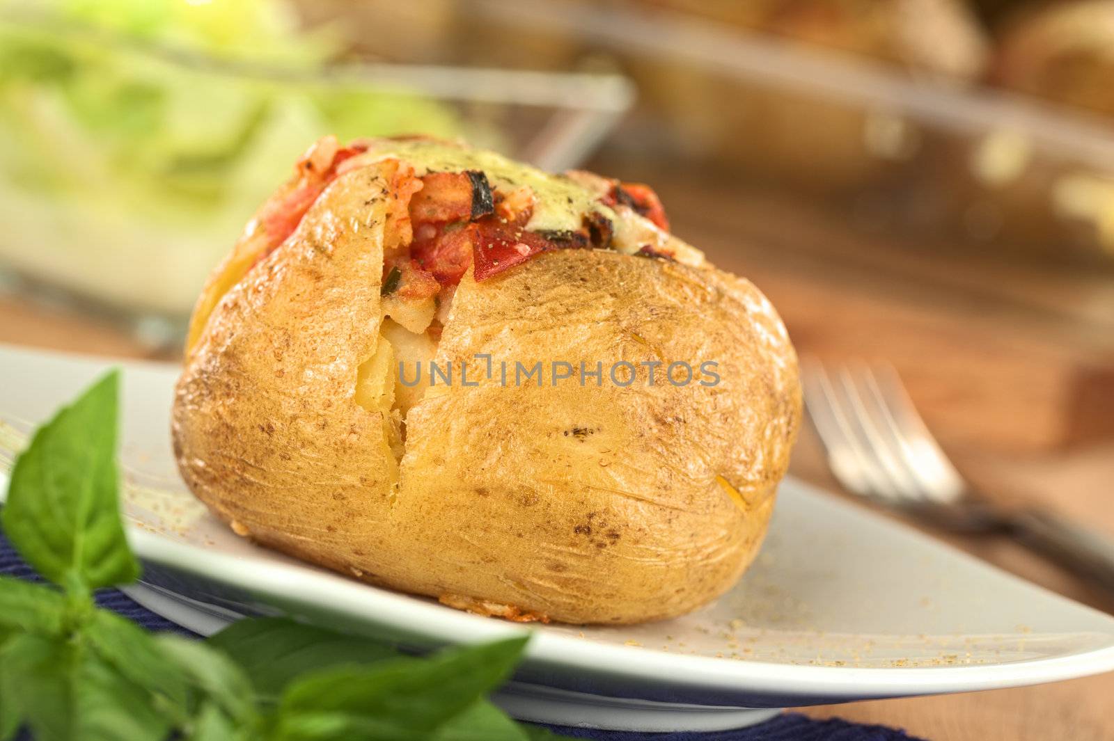 Baked potato with tomato filling and cheese on top (Selective Focus, Focus on the front of potato)