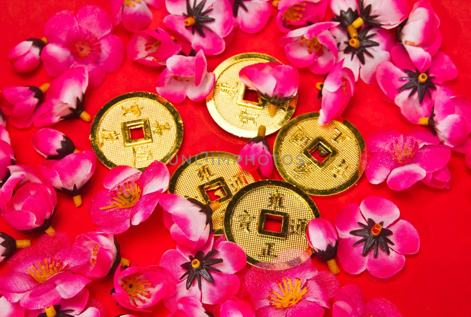Golden coins ornaments with plastic cherry blossoms on red surface for CNY celebration