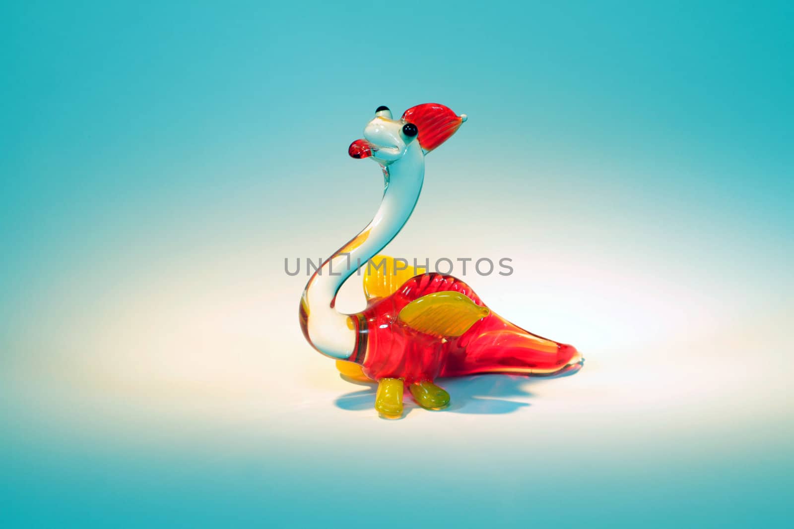 glass figurine of smiling yellow and red dragon in a spotlight on turquoise background