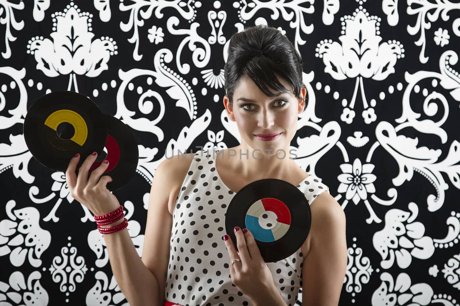 young woman is stylist 60's inspired clothing, showing off three vinyl records