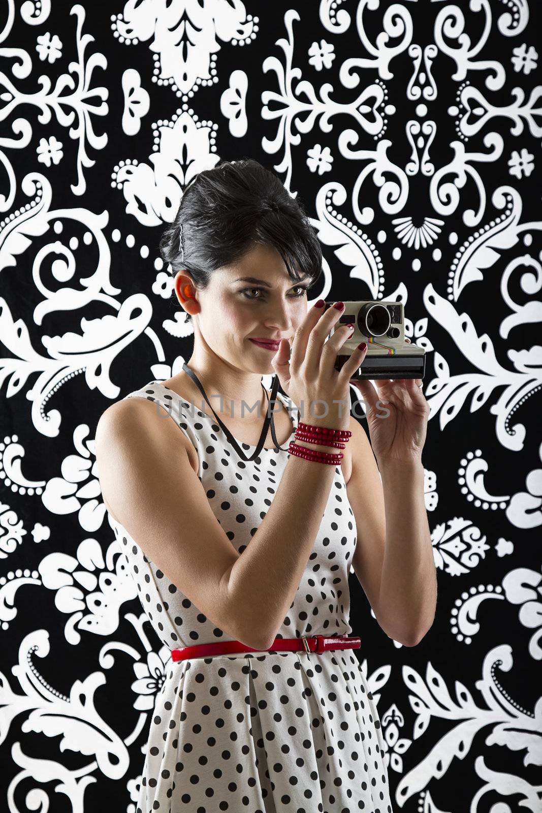 young woman is stylist 60's inspired clothing, holding an instant camera and preparing to take a photo