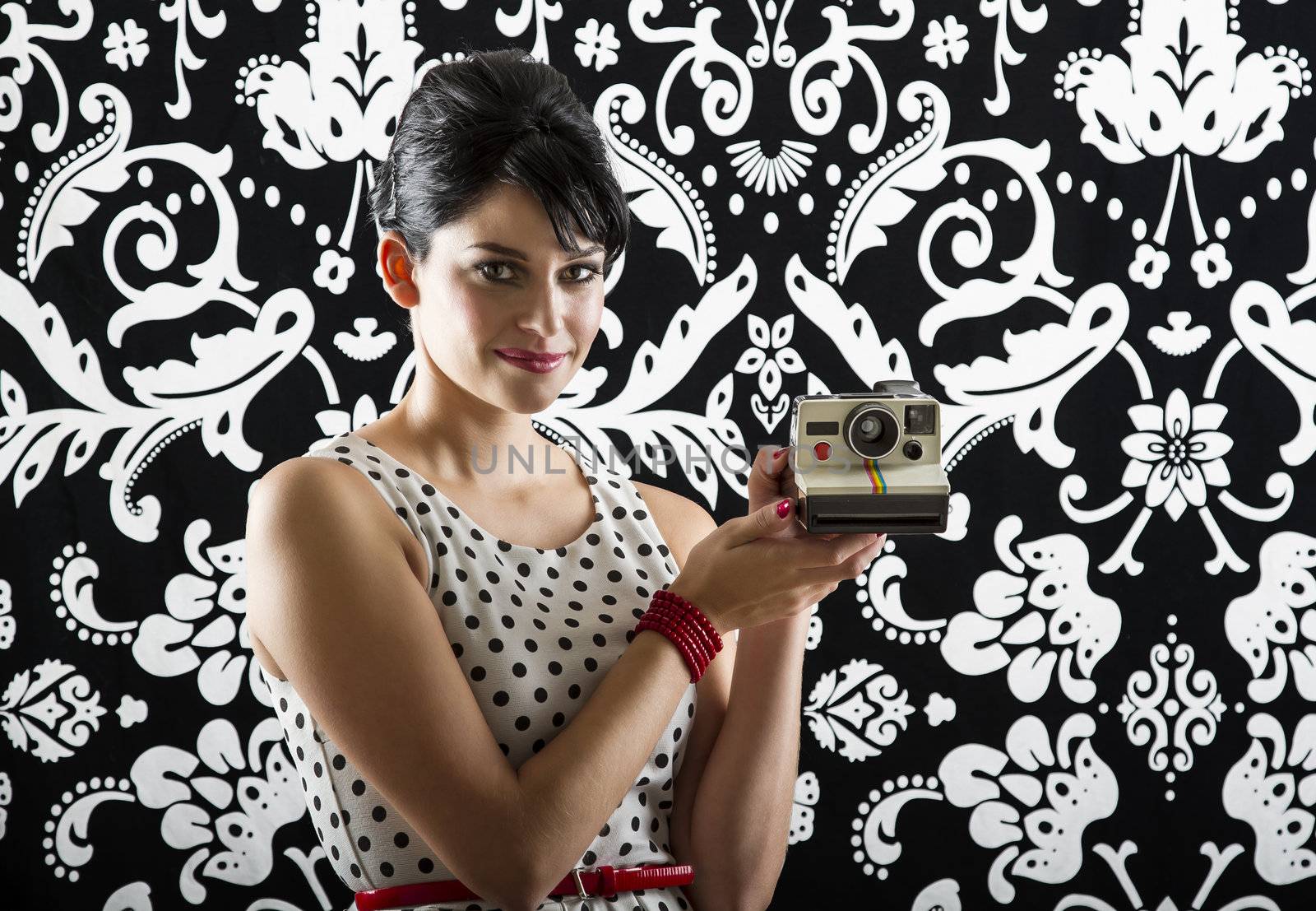 young woman is stylist 60's inspired clothing, presenting an instant camera