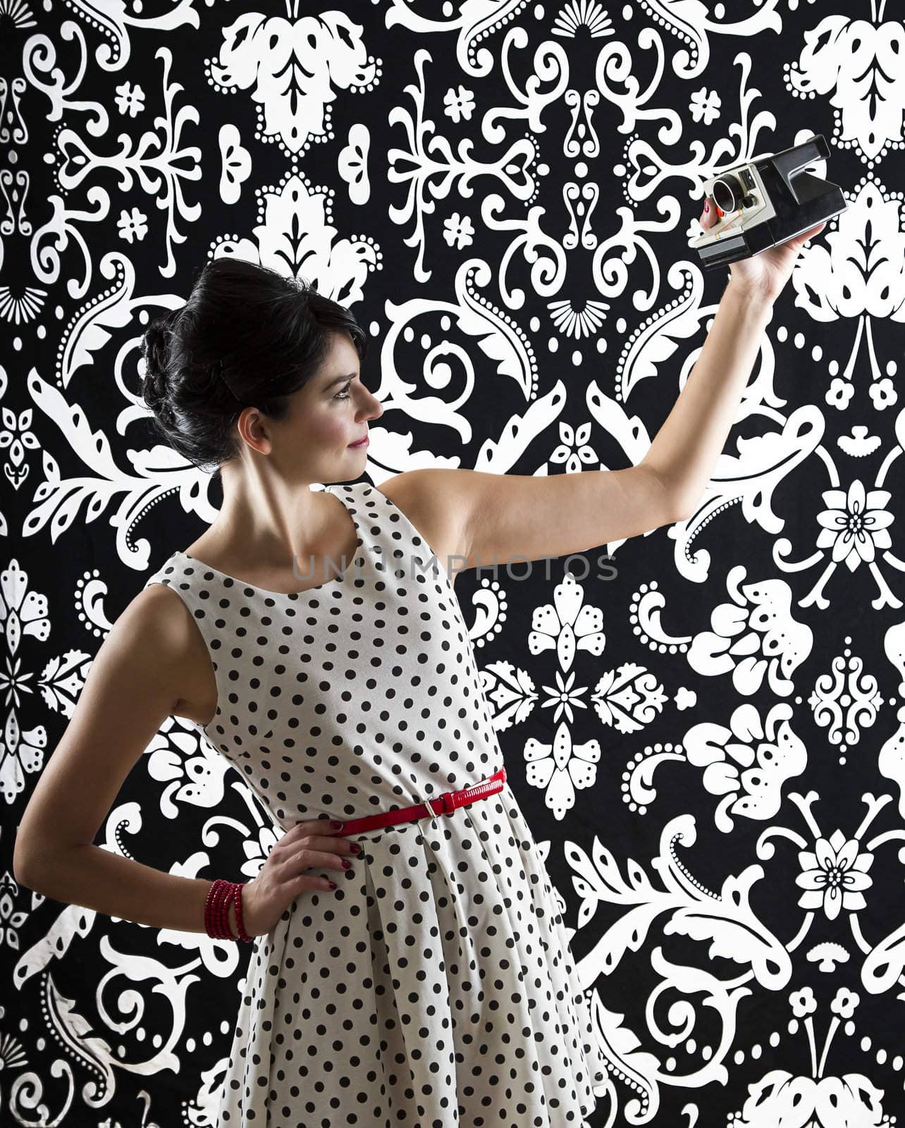 young woman is stylist 60's inspired clothing, taking a self-portrait with an instant camera
