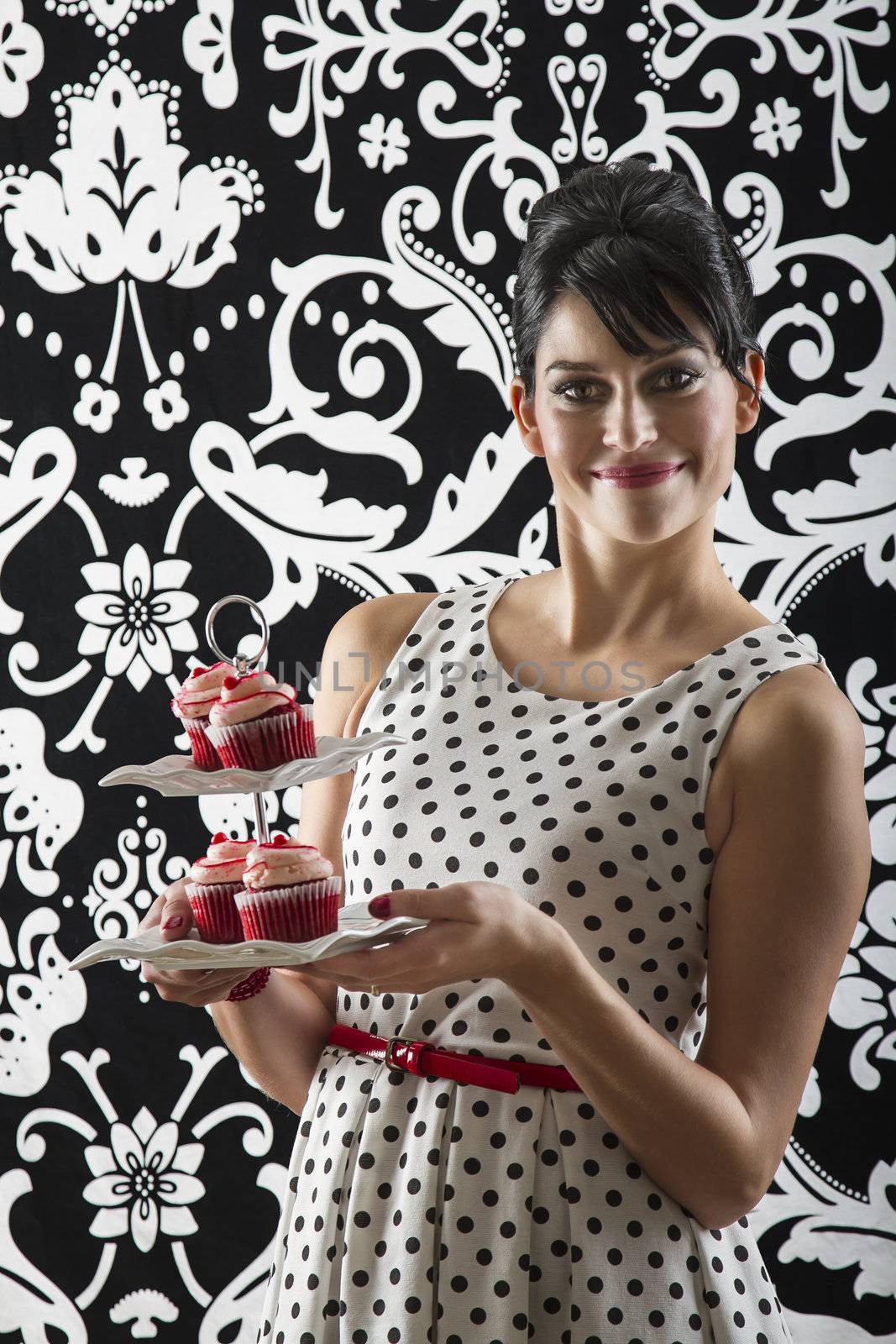 young woman is stylist 60's inspired clothing, serving a plate of velvet cupcake