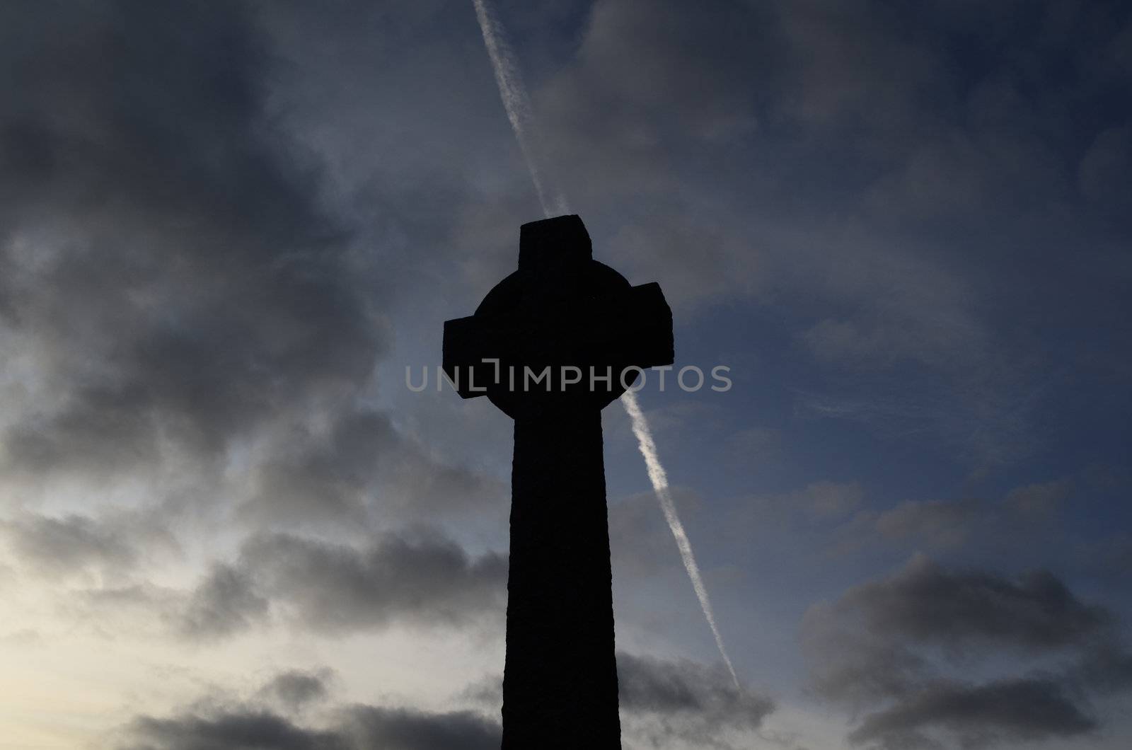 Sillouette of cross against coudy sky with airoplane trail