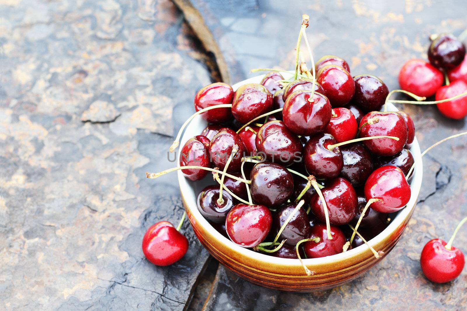 Bowl of black cherries with stems over a rustic background with available copy space.