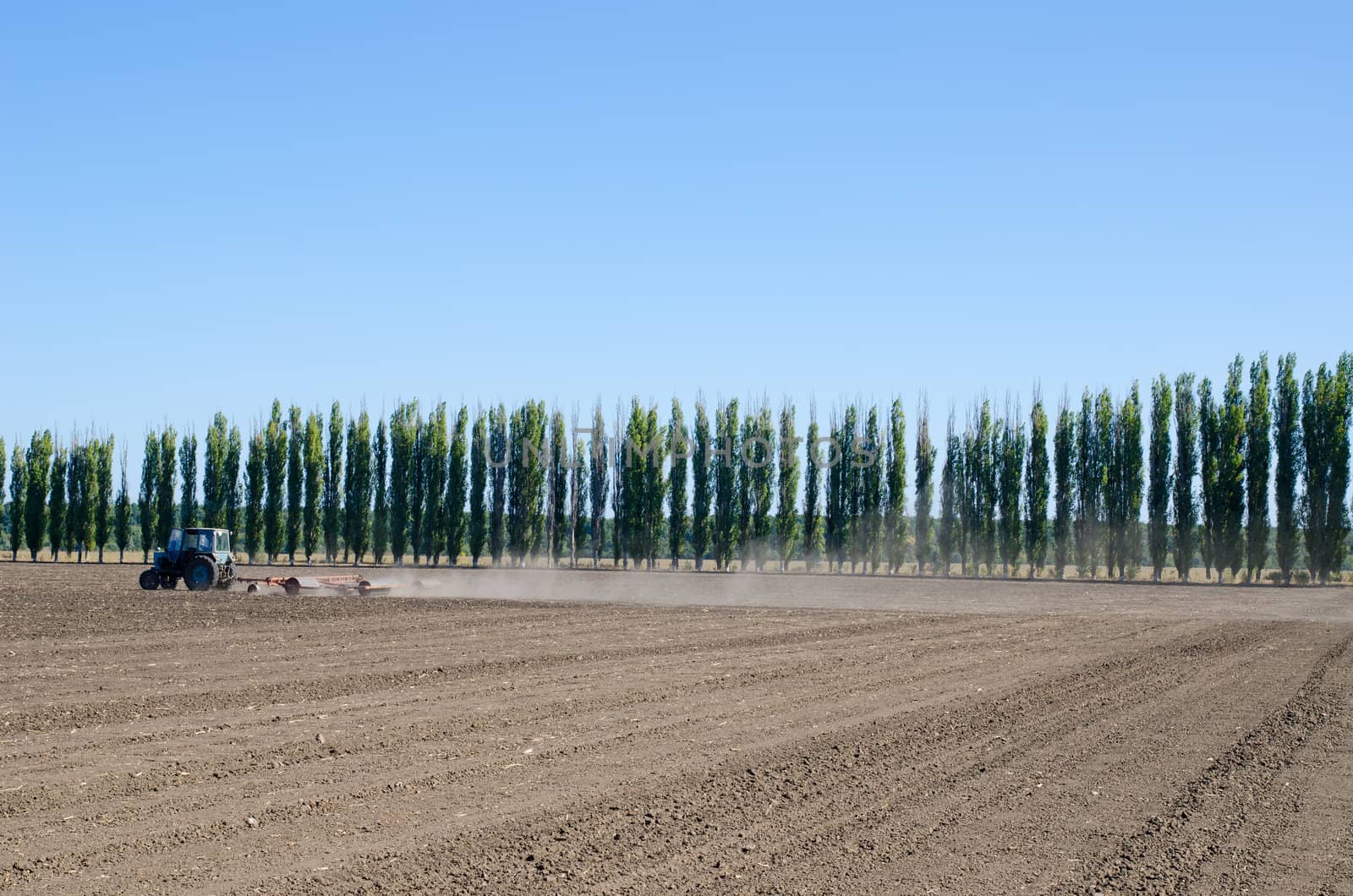 agriculture tractor on black ploughed field under blue sky