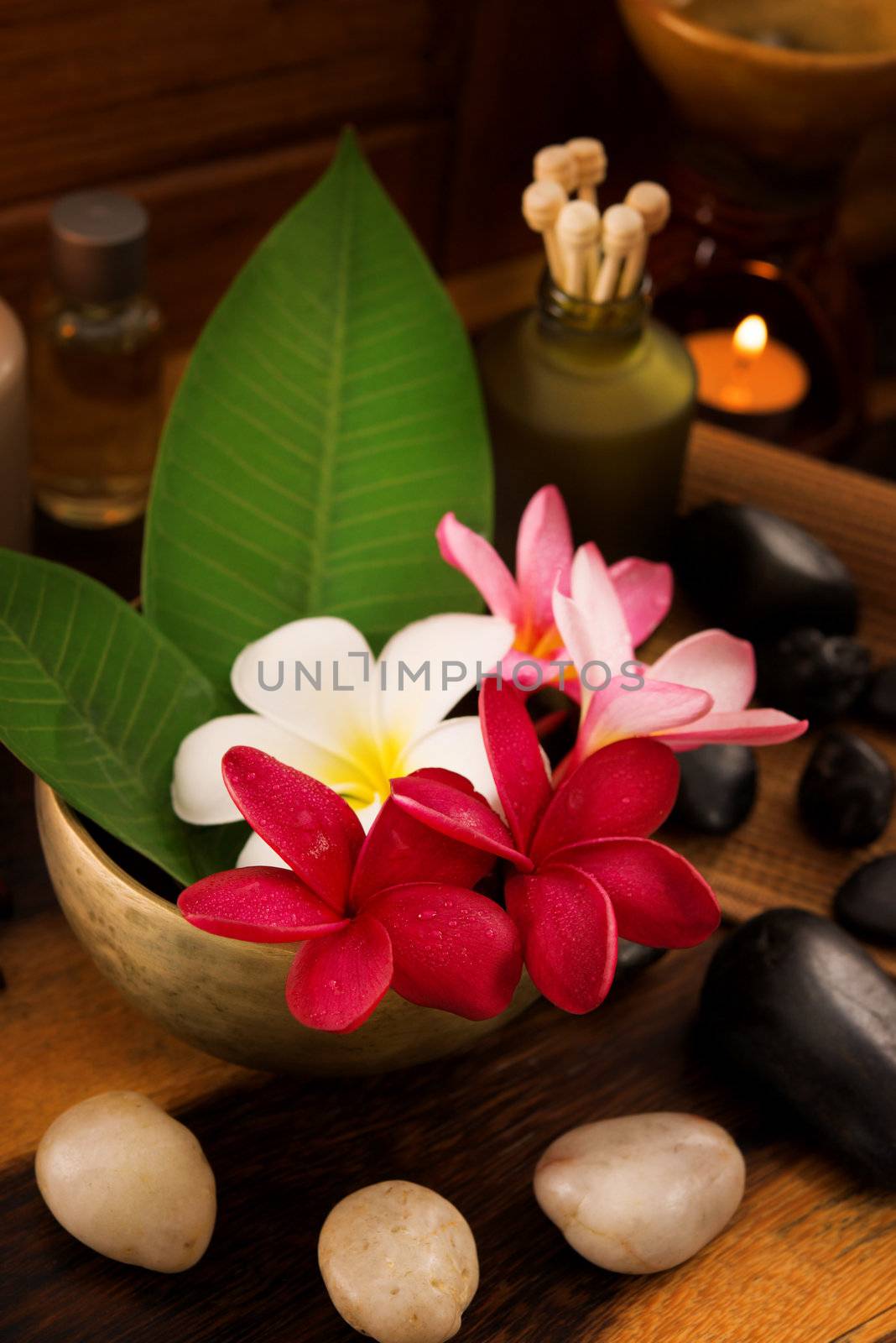 Spa still life setting with aromatic candles, frangipani flower, cold and hot stones.