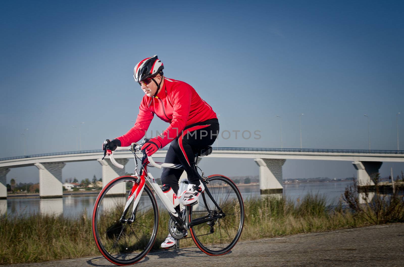 Man on road bike riding down open country road, bridge on background.