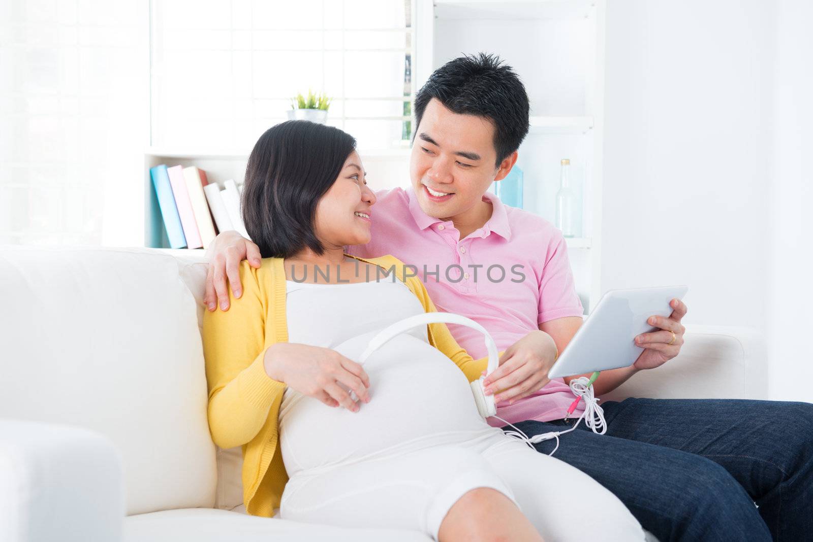 Pregnant woman putting headphones on her belly. Asian pregnant couple living lifestyle.