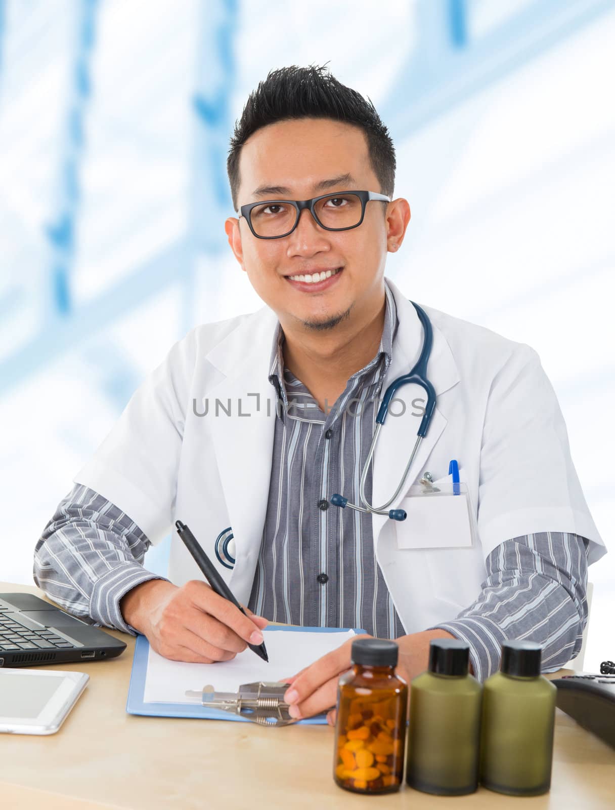 Young Southeast Asian medical doctor working on his desk, inside hospital room.