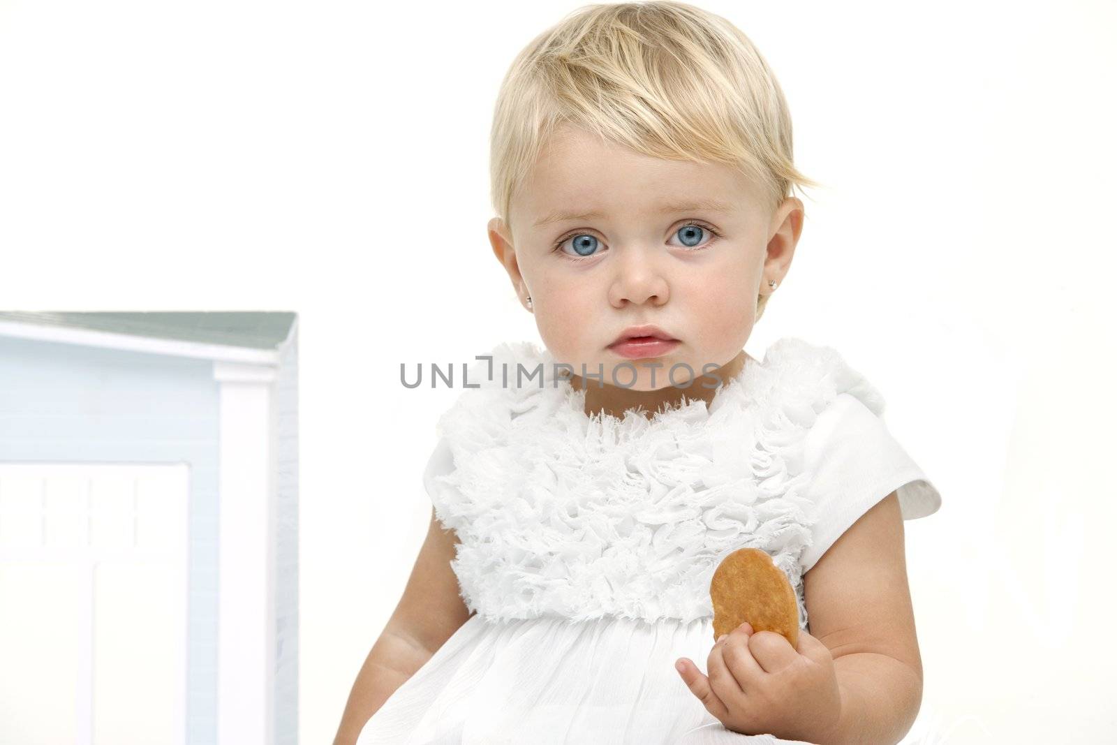 Blue eyed baby girl with boring expression holding a biscuit. Isolated on white background.