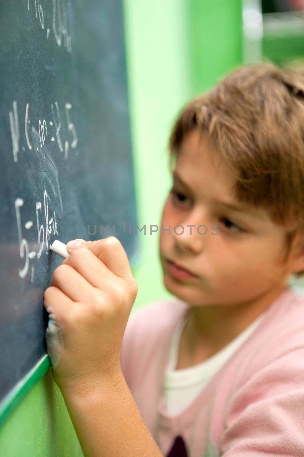 Close up of young student writing with chalk on chalkboard in classroom