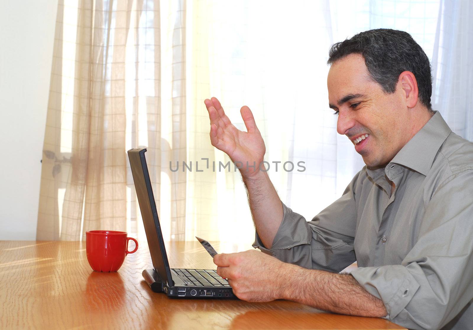 Man sitting at his desk with laptop holding a credit card looking happy