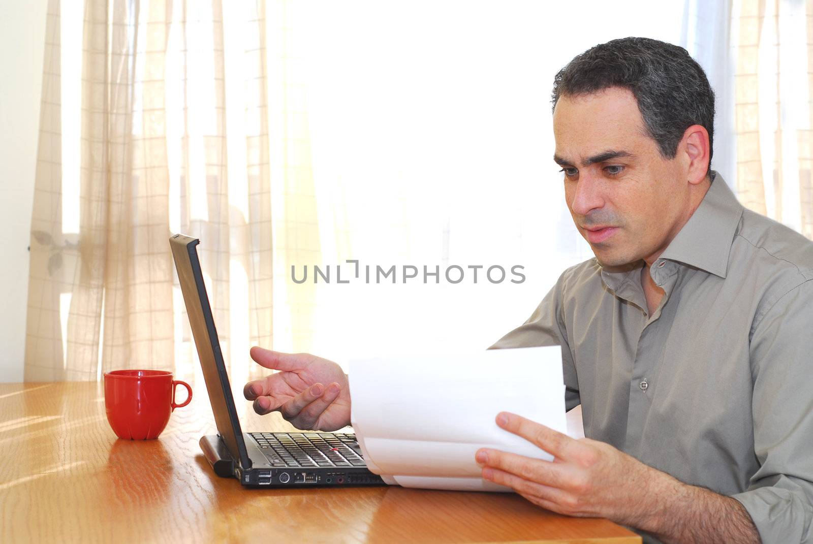 Man sitting at his desk with a laptop looking at bills