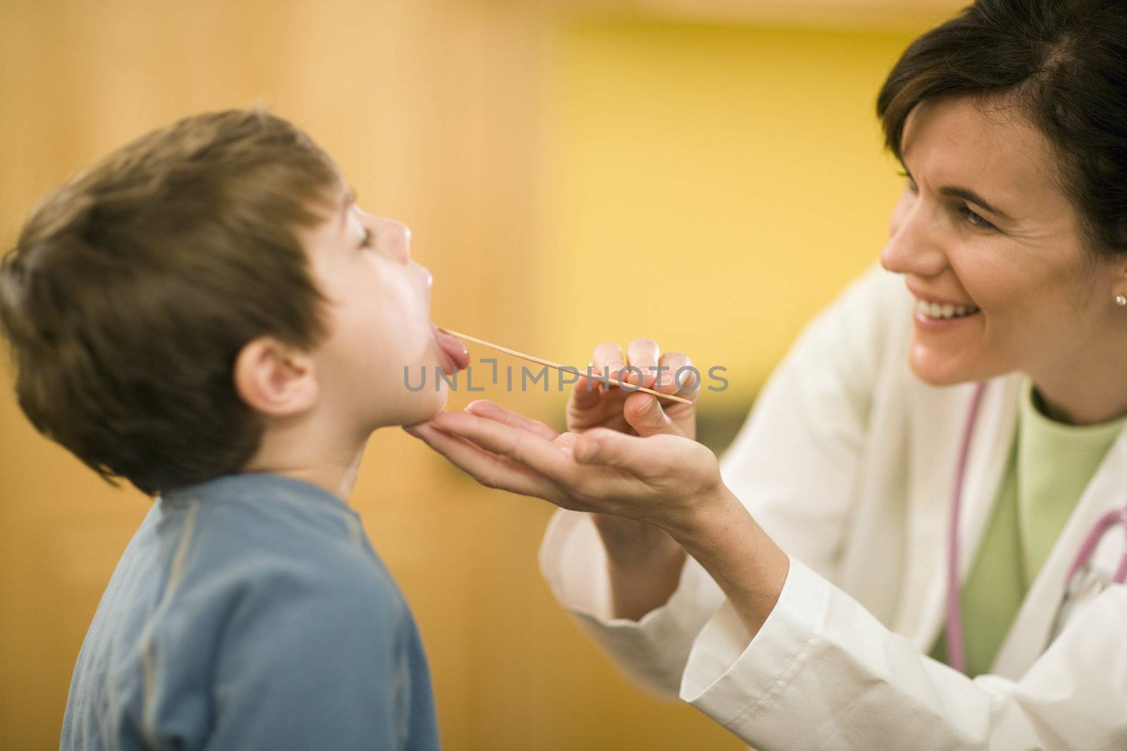 Smiling woman doctor examining child patient with tongue depressor