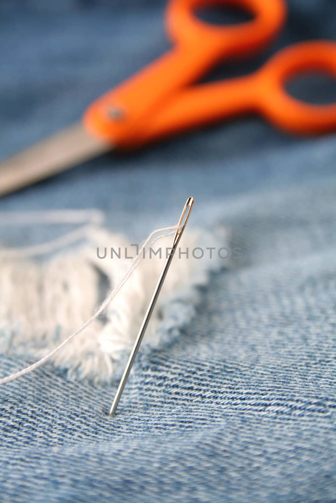 Close up of a needle and thread with scissors in the background.